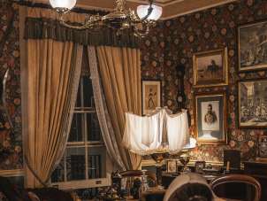 A reconstructed interior at the Sherlock Holmes Museum, featuring a desk, armchairs, a rug, lamps, and display cases. Historical paintings and decorations hang on the walls. The room is designed in the style of a Victorian study.