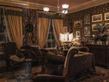 A reconstructed interior at the Sherlock Holmes Museum, featuring a desk, armchairs, a rug, lamps, and display cases. Historical paintings and decorations hang on the walls. The room is designed in the style of a Victorian study.