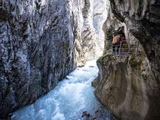 Der Fluss formte die Rosenlaui Gletscherschlucht über Jahrhunderte. Der Weg führt an der Felswand über dem Fluss in die Schlucht hinein. Die zwei Wanderer bestaunen den Fluss in der Rosenlauischlucht vom Steg aus.