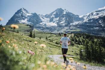 Un coureur sur le parcours de montagne du marathon de la Jungfrau. À l'arrière-plan, on aperçoit le trio formé par l'Eiger, le Mönch et la Jungfrau.