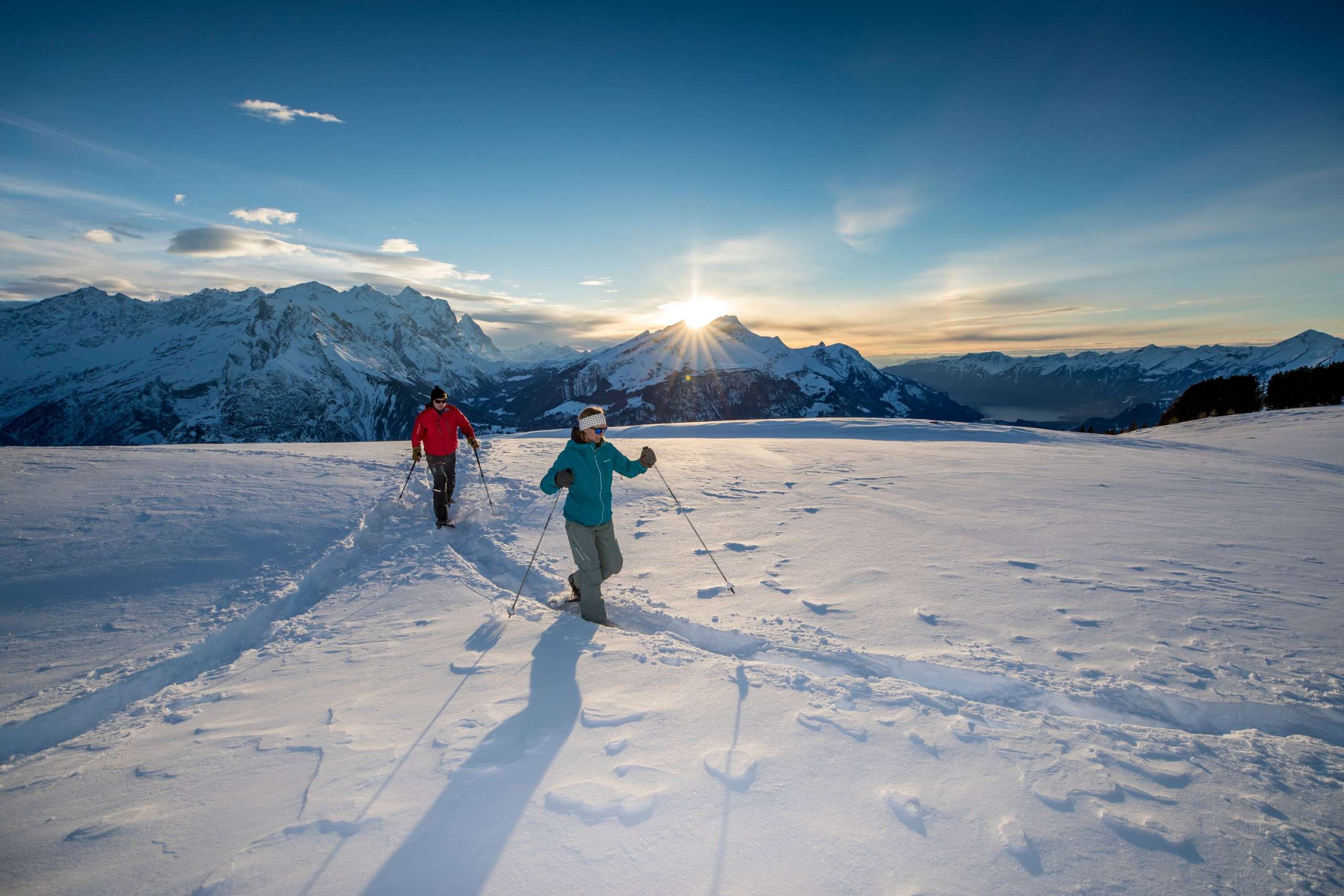 Au coucher du soleil, avec pour toile de fond un impressionnant paysage montagneux : deux randonneurs en raquettes sur le Hasliberg
