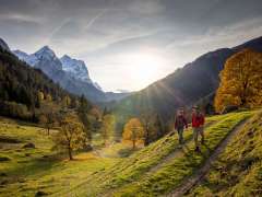 Two hikers are out walking in the Rosenlaui Valley countryside. There is an autumnal atmosphere, and the sky is covered with a light haze. The mountain panorama is cloaked in snow.