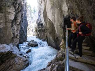 Der Fluss formte die Rosenlaui Gletscherschlucht über Jahrhunderte. Der Weg führt an der Felswand über dem Fluss in die Schlucht hinein. Die zwei Wanderer bestaunen den Fluss in der Rosenlauischlucht vom Steg aus.