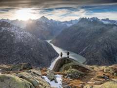 Two hikers on the trail in the Grimsel region. They are hiking with a breathtaking view of a reservoir in the Grimsel region.
