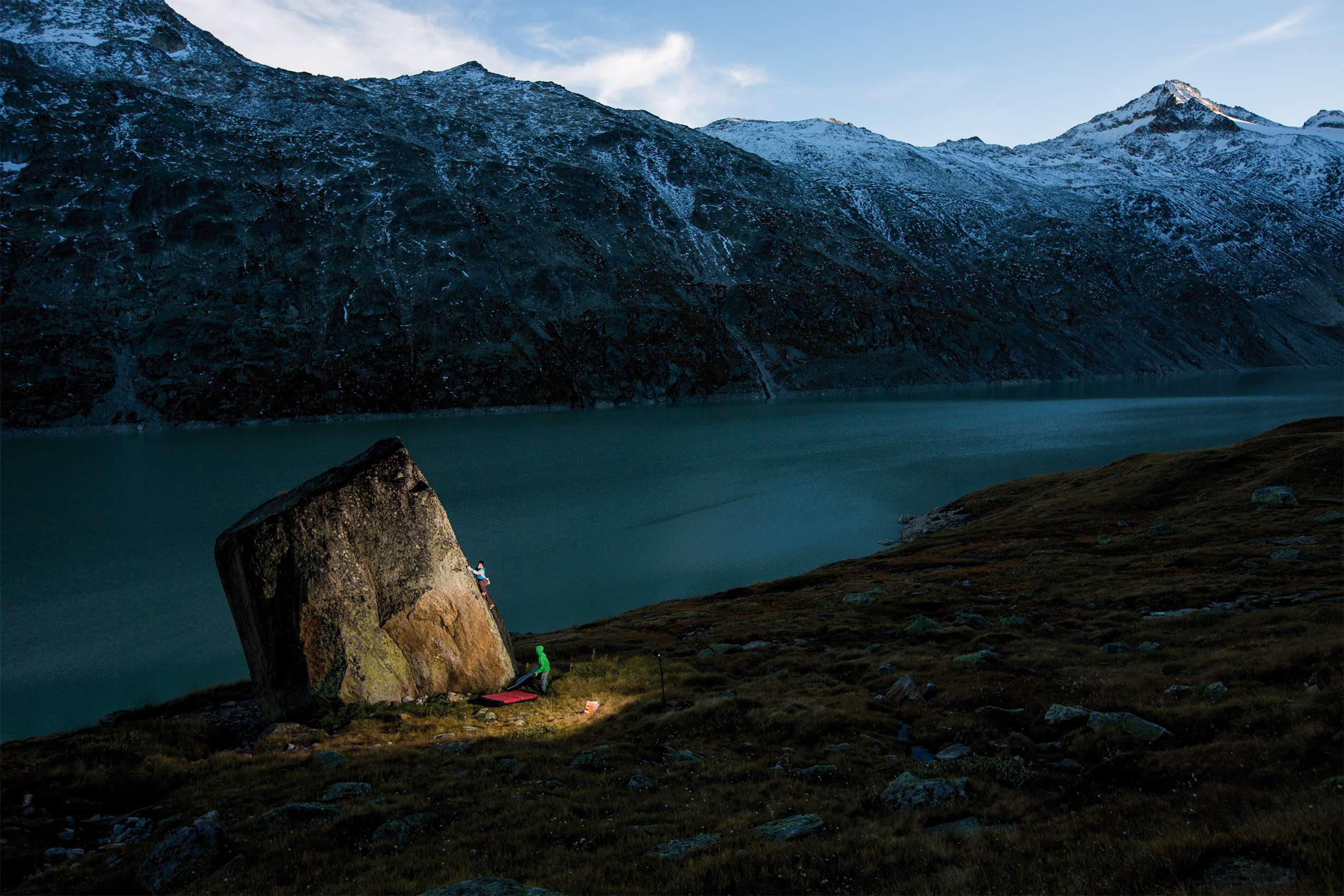 Deux grimpeurs sur un rocher d'escalade au crépuscule avec un lac et des montagnes en arrière-plan.