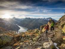 Zwei Wanderer unterwegs in der Grimselwelt.  Sie wandern  vor einmaliger Aussicht auf den Grimsel Stausee in der  Grimselwelt. Auf dem Wanderweg zwischen dem Grimselpass und dem Nägelisgrätli.