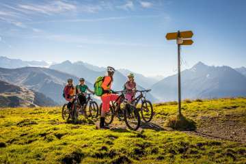 The cyclists look at the signpost and enjoy the view from Hasliberg. The view offers a summery panorama of the mountain landscape.