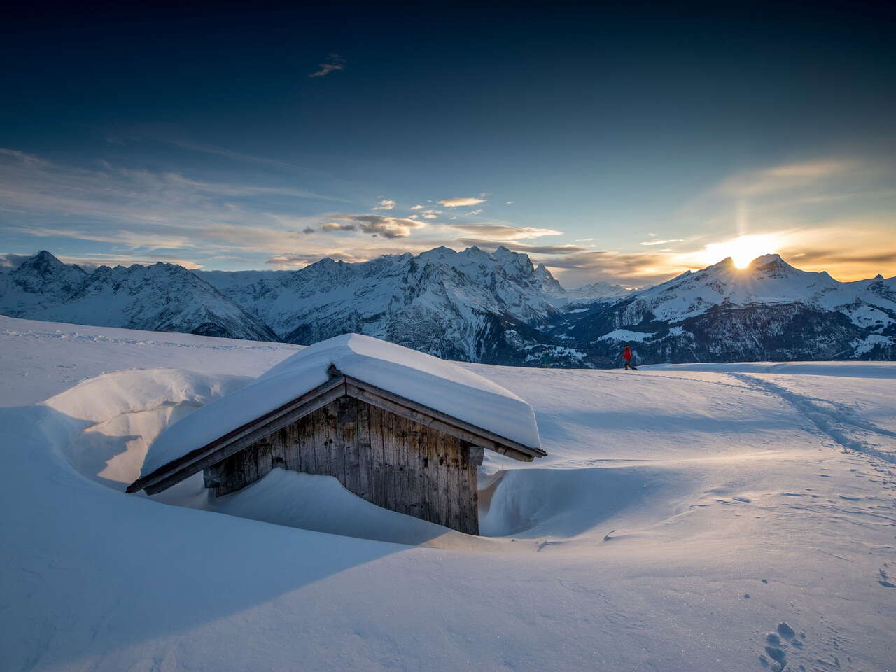 A lone hiker out and about at sunset in the snowy winter landscape on the Hasliberg