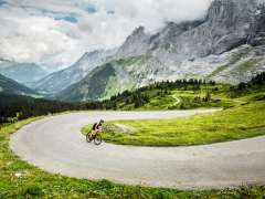 Riding a road bike on a road on the Grosse Scheidegg. In the background, the valley stretches out, and the mountain ridges hold back the clouds.
