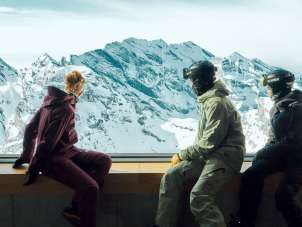 Three people are enjoying the panoramic view from the Birg station. Through the Piz Gloria Frames, an impressive view of the snow-covered mountains unfolds.