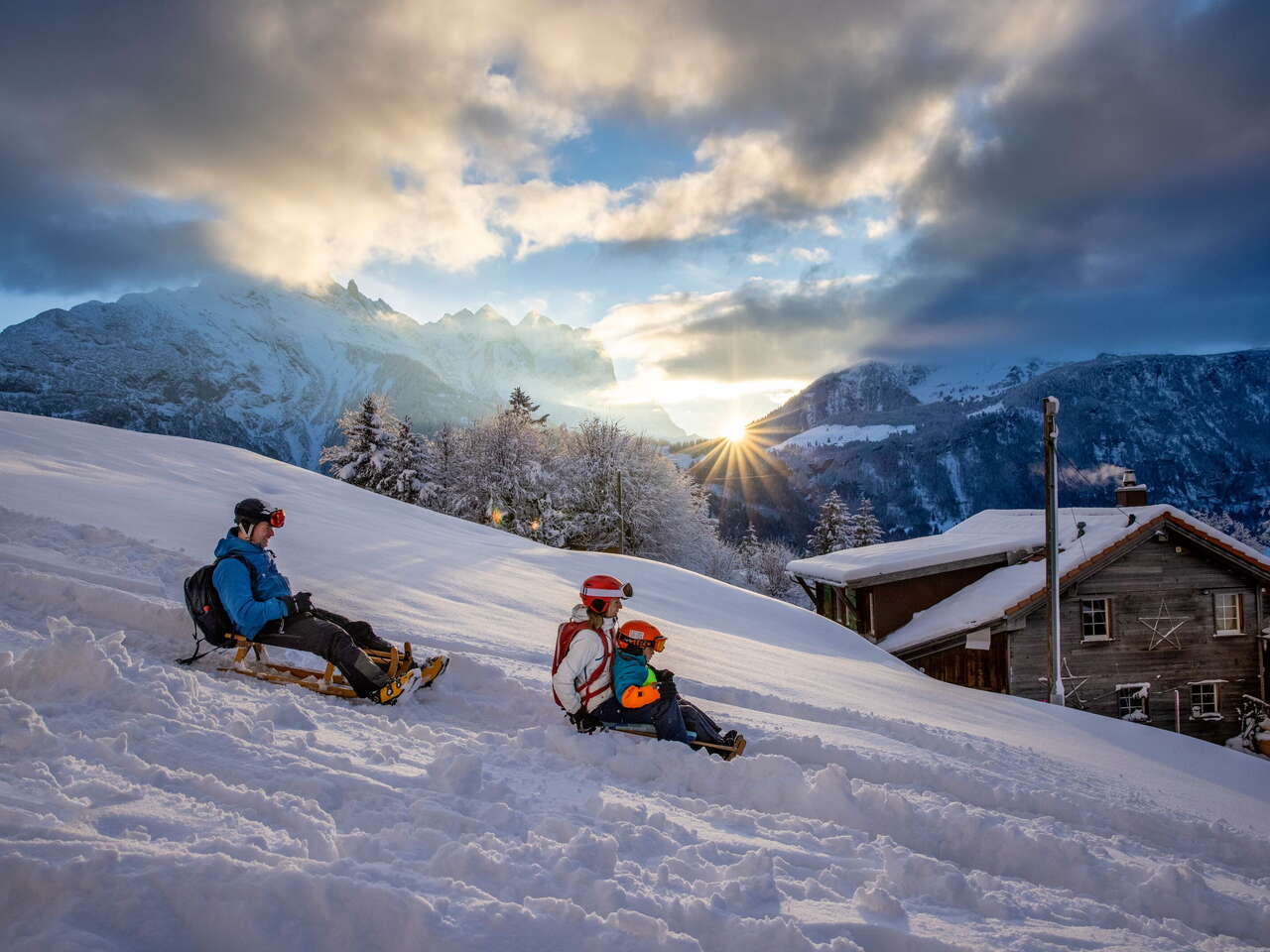 Au coucher du soleil : une jeune famille fait de la luge sur le Hasliberg.