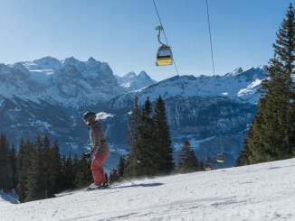 Skifahrerin unterwegs im Skigebiet Meiringen-Hasliberg. Über ihr verkehrt die Gondelbahn der Bergbahnen Meiringen-Hasliberg. Im Hintergrund die eindrückliche Bergwelt des Haslitals.