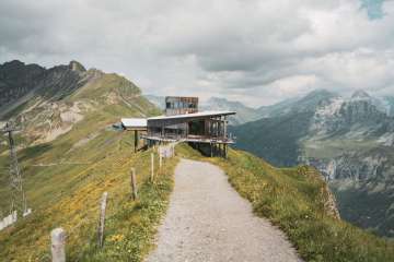 The Alpen Tower stands on the mountain ridge. It's slightly cloudy, but the sun is casting a few rays of sunlight onto the trail.