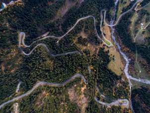 This aerial view of the Grimsel Pass shows many sharp curves. The road is surrounded by a fir forest.