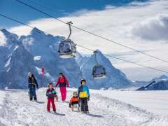 Winter in the Haslital Valley: A young family sledding on the Hasliberg. In the background are the gondolas of the Meiringen-Hasliberg mountain railways—and the impressive mountain scenery of the Haslital Valley.