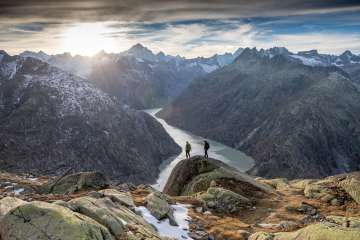 Deux randonneurs en route dans le massif du Grimsel. Ils marchent devant un panorama unique sur un lac de barrage du massif du Grimsel.