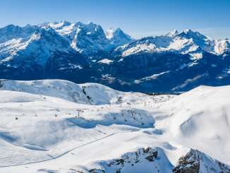 Le paysage enneigé du Hasliberg s'étend sur des collines et des pentes douces. Au centre de l'image, en contrebas, se trouve la Mägisalp avec ses bâtiments, tandis qu'à l'arrière-plan, on aperçoit l'Eiger, le Wetterhorn, la Grosse Scheidegg et d'autres sommets.