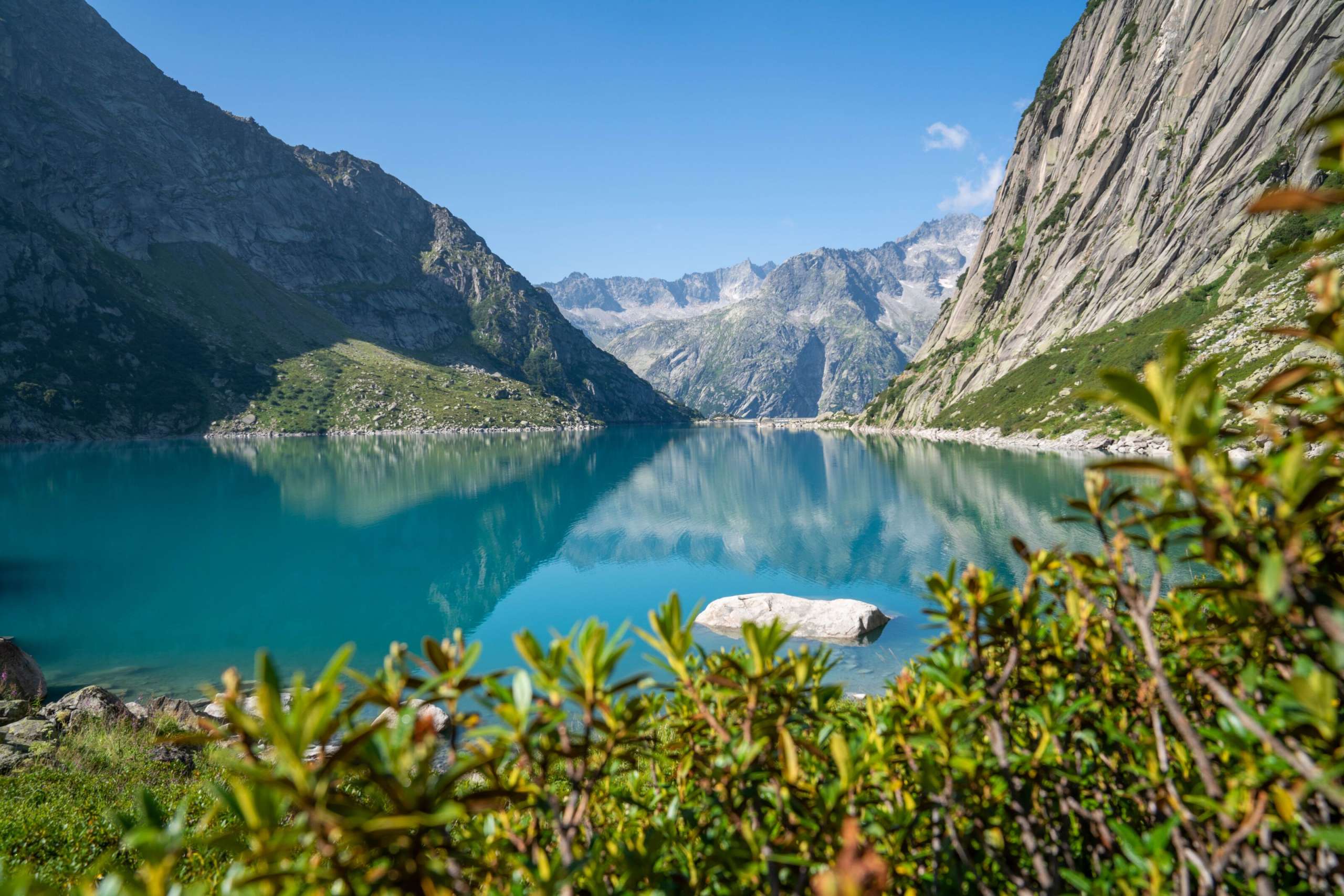 Nahaufnahme vom Gelmersee. Das türkisfarbene Wasser spiegelt die umliegenden Berggipfel auf der Wasseroberfläache.