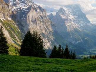 Panoramablick von der Grossen Scheidegg über grüne Alpweiden auf Mättenberg, Eiger und das Tal von Grindelwald unter einem wolkigen Himmel.