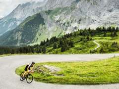 Riding a road bike on a road on the Grosse Scheidegg. In the background, the valley stretches out, and the mountain ridges hold back the clouds.