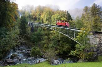 Die rote Reichenbachfall-Bahn fährt über die Brücke hoch zum Reichenbach.