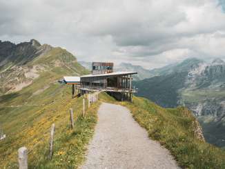 L'Alpen Tower se dresse sur la crête de la montagne. Le ciel est légèrement nuageux, mais le soleil laisse percer quelques rayons sur le sentier.