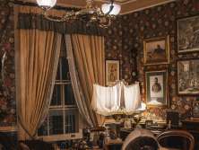 A reconstructed interior at the Sherlock Holmes Museum, featuring a desk, armchairs, a rug, lamps, and display cases. Historical paintings and decorations hang on the walls. The room is designed in the style of a Victorian study.
